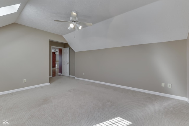 additional living space featuring vaulted ceiling with skylight, light colored carpet, and baseboards