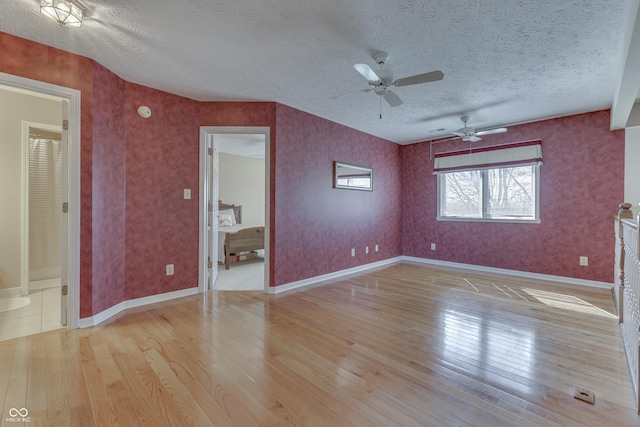 unfurnished bedroom featuring wallpapered walls, light wood-style flooring, baseboards, and a textured ceiling