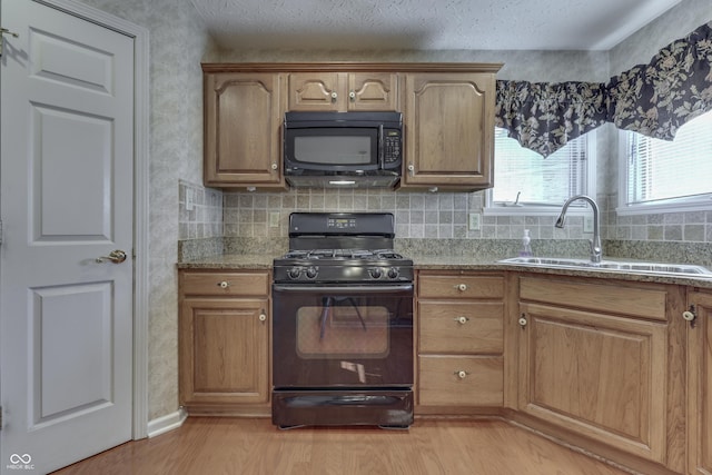 kitchen with backsplash, light stone countertops, light wood-style floors, black appliances, and a sink