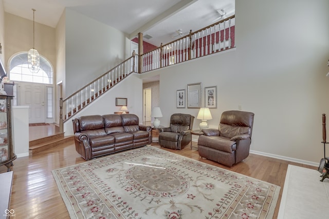 living room featuring a notable chandelier, stairway, a towering ceiling, and wood finished floors