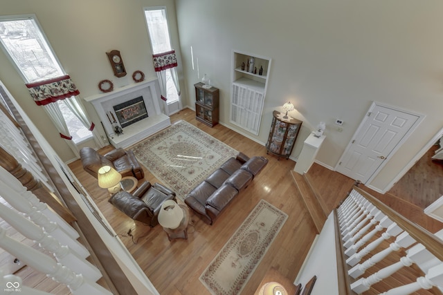 living area featuring a premium fireplace, a healthy amount of sunlight, wood finished floors, and a towering ceiling