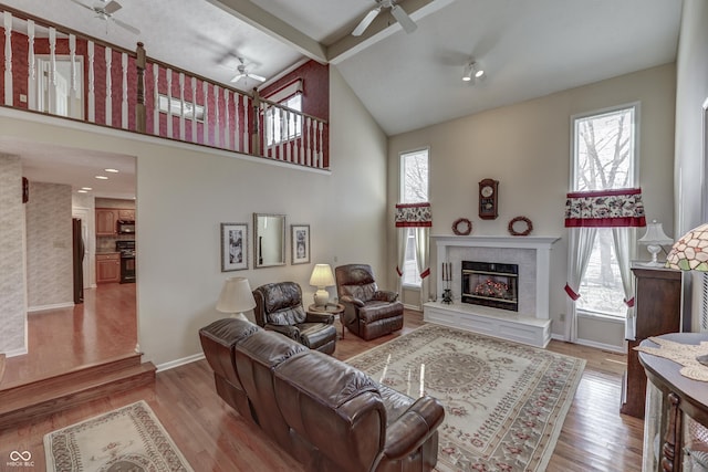 living room featuring beam ceiling, a fireplace, a ceiling fan, and wood finished floors