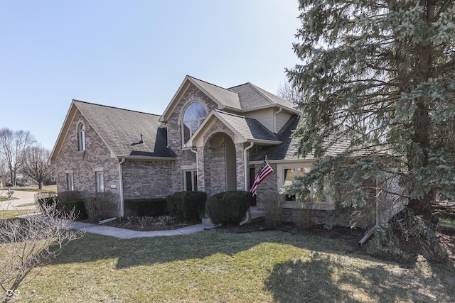 view of front of property with a front lawn, brick siding, and roof with shingles