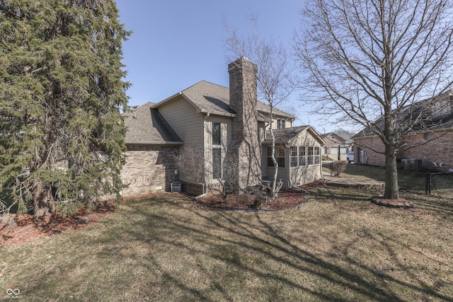 view of home's exterior with a lawn, fence, a shingled roof, brick siding, and a chimney