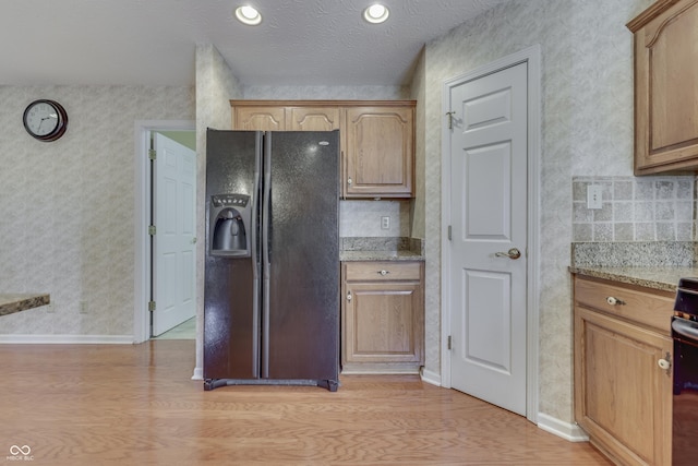 kitchen featuring light stone counters, black fridge, light wood-style flooring, and baseboards