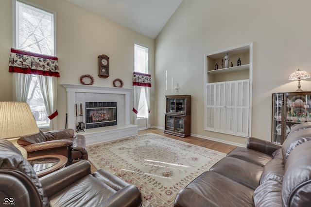 living room with a tiled fireplace, high vaulted ceiling, a wealth of natural light, and wood finished floors