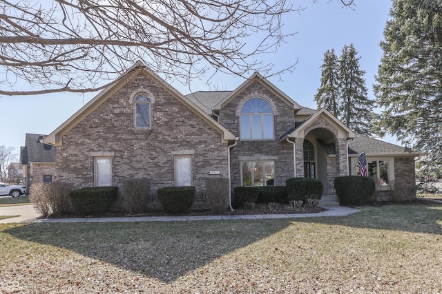 view of front of property featuring a front lawn, brick siding, and roof with shingles