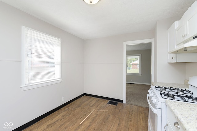 kitchen with visible vents, baseboards, white gas stove, light countertops, and white cabinetry