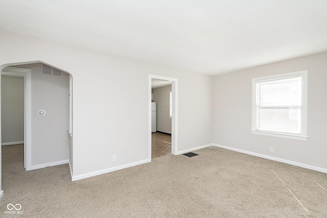 unfurnished bedroom with arched walkways, baseboards, freestanding refrigerator, and carpet