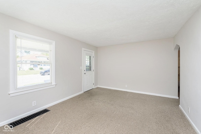 spare room with arched walkways, visible vents, carpet, and a wealth of natural light