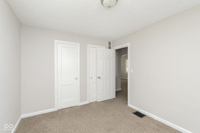 unfurnished bedroom featuring visible vents, baseboards, light colored carpet, and a textured ceiling