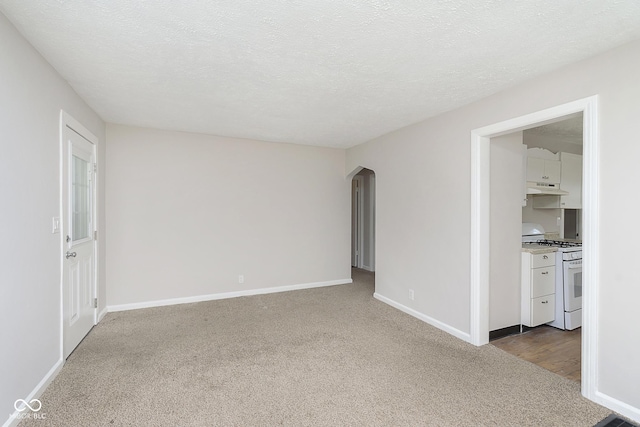 carpeted empty room with baseboards, arched walkways, and a textured ceiling