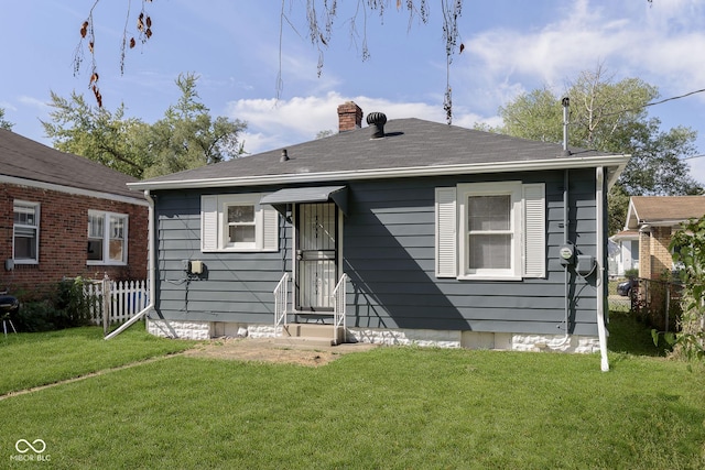 back of property with a shingled roof, a chimney, a yard, and fence