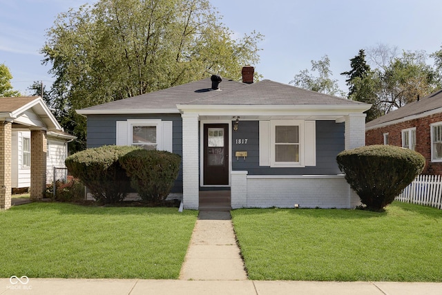 bungalow-style home featuring brick siding, a shingled roof, a front lawn, fence, and a chimney