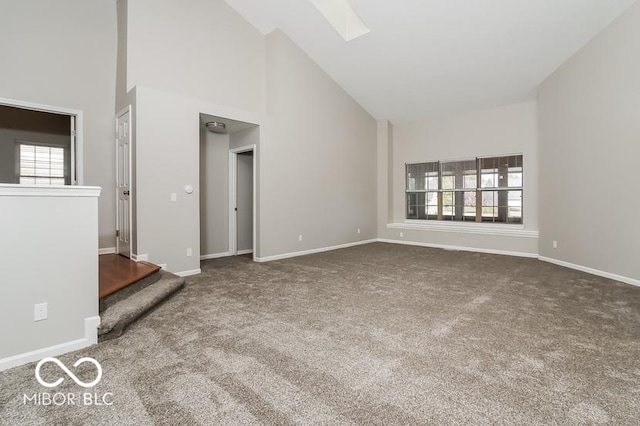 unfurnished living room featuring baseboards, high vaulted ceiling, a skylight, and carpet flooring