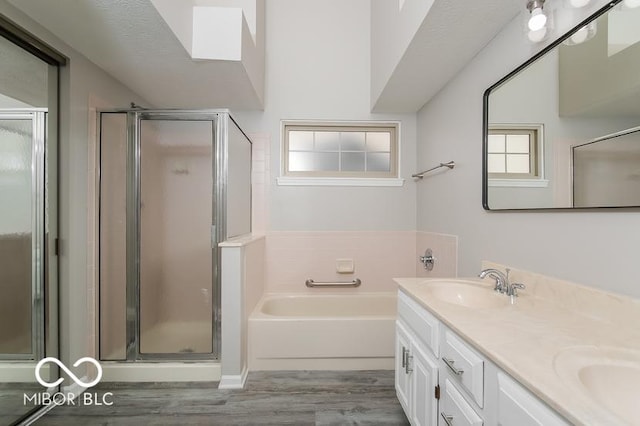 bathroom featuring a sink, wood finished floors, a shower stall, double vanity, and a bath