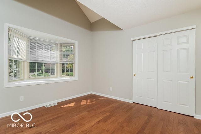 unfurnished bedroom featuring visible vents, baseboards, vaulted ceiling, wood finished floors, and a closet