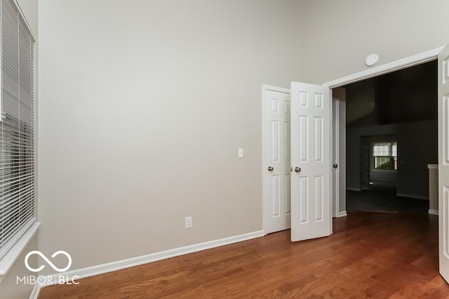 unfurnished bedroom featuring a high ceiling, baseboards, and wood finished floors