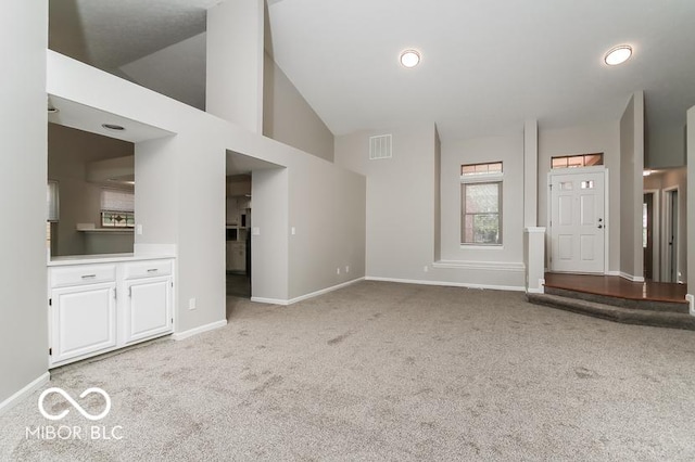 unfurnished living room with baseboards, light colored carpet, visible vents, and high vaulted ceiling