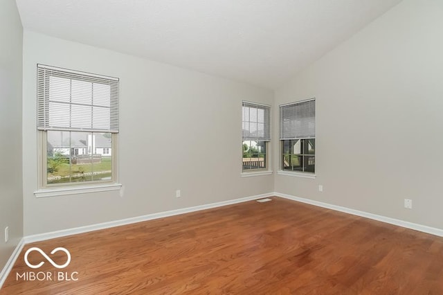 spare room featuring baseboards, lofted ceiling, and wood finished floors