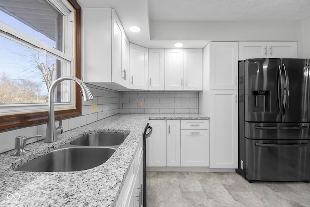 kitchen featuring a sink, backsplash, refrigerator with ice dispenser, and white cabinetry