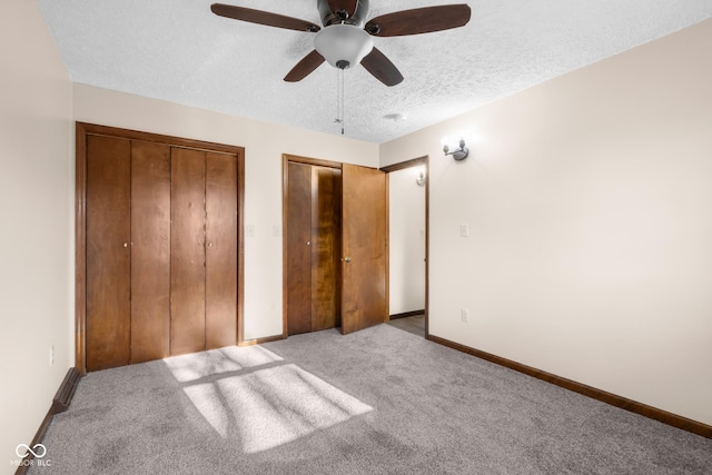 unfurnished bedroom featuring multiple closets, a ceiling fan, a textured ceiling, carpet floors, and baseboards