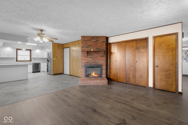 unfurnished living room featuring a fireplace, wood finished floors, a textured ceiling, a ceiling fan, and a sink