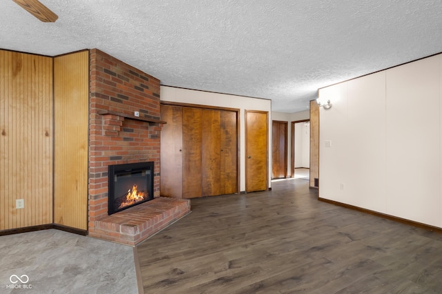 unfurnished living room with a brick fireplace, wooden walls, wood finished floors, and a textured ceiling