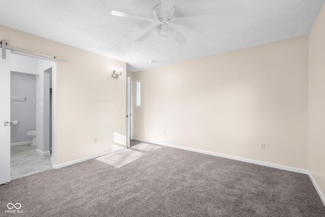 carpeted spare room with a barn door, baseboards, a textured ceiling, and a ceiling fan