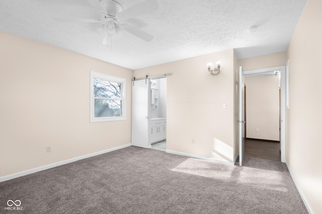 unfurnished bedroom with a barn door, carpet flooring, a textured ceiling, and baseboards