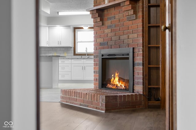 interior details with decorative backsplash, a brick fireplace, wood finished floors, and a sink