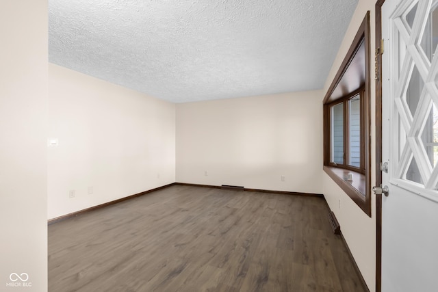 unfurnished room with a textured ceiling, baseboards, and wood finished floors