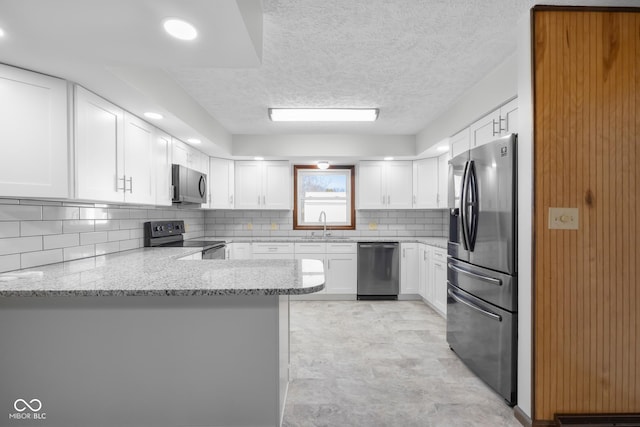 kitchen featuring light stone countertops, a peninsula, white cabinets, appliances with stainless steel finishes, and backsplash