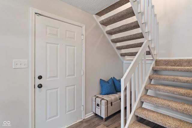 staircase featuring a textured ceiling, baseboards, and wood finished floors