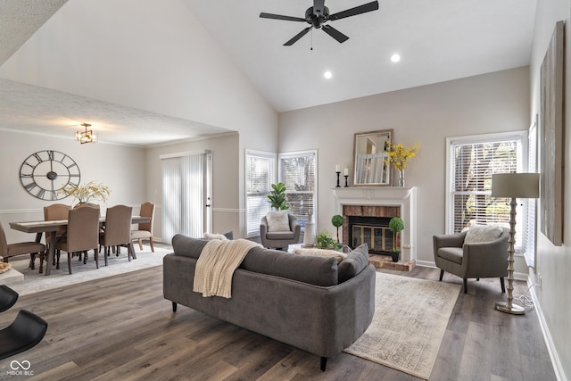 living area featuring a brick fireplace, a healthy amount of sunlight, dark wood-style flooring, and high vaulted ceiling