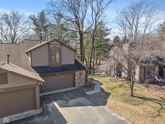 view of front facade with a front lawn, aphalt driveway, stone siding, an attached garage, and a shingled roof