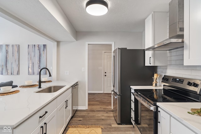 kitchen with wall chimney range hood, white cabinets, appliances with stainless steel finishes, and a sink