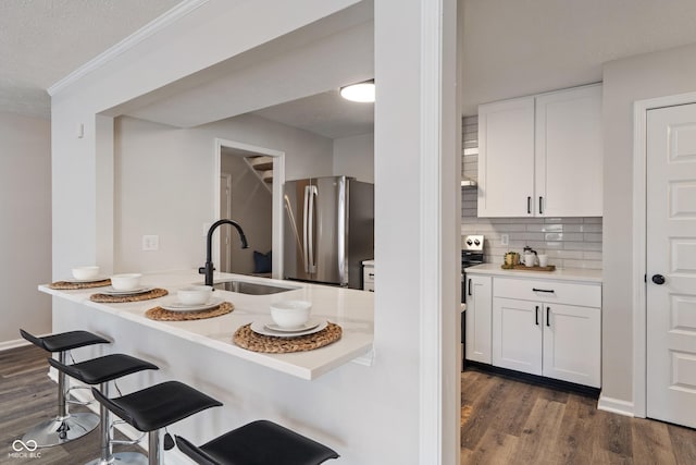 kitchen with a kitchen bar, a sink, dark wood-style floors, white cabinetry, and freestanding refrigerator