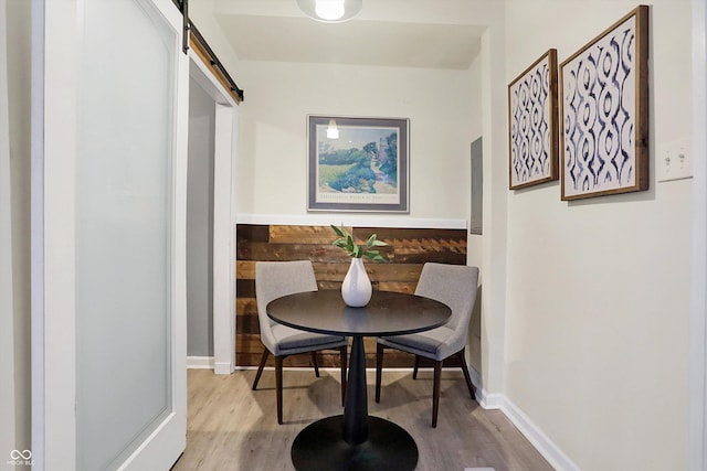 dining room featuring a barn door, baseboards, and wood finished floors