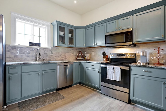 kitchen with light wood finished floors, glass insert cabinets, decorative backsplash, appliances with stainless steel finishes, and a sink