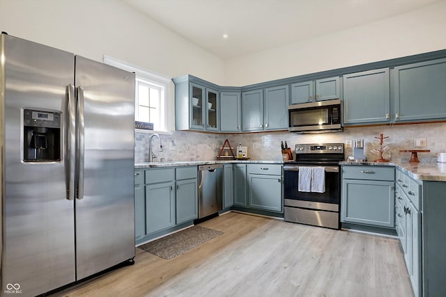 kitchen with a sink, decorative backsplash, light wood-style flooring, and stainless steel appliances