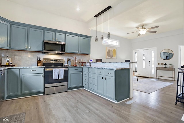 kitchen featuring decorative light fixtures, stainless steel appliances, light wood-style floors, a peninsula, and decorative backsplash