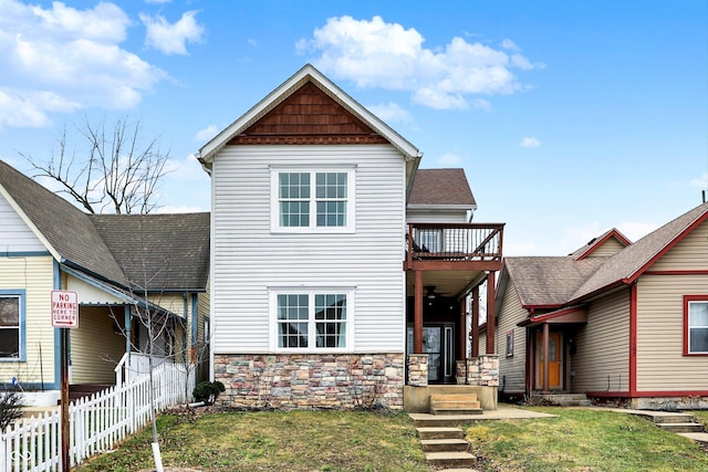 view of front of property with stone siding, roof with shingles, a front lawn, and fence