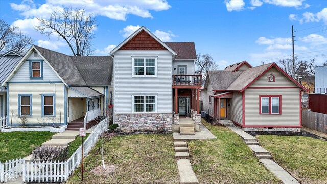 view of front of property with a front yard, fence, stone siding, and a shingled roof