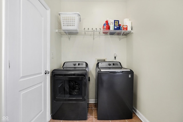 clothes washing area with light tile patterned floors, baseboards, washing machine and dryer, and laundry area