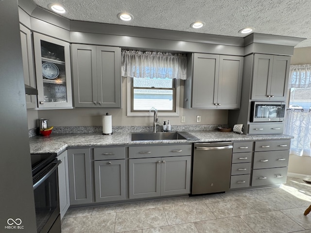 kitchen with appliances with stainless steel finishes, a textured ceiling, gray cabinetry, and a sink