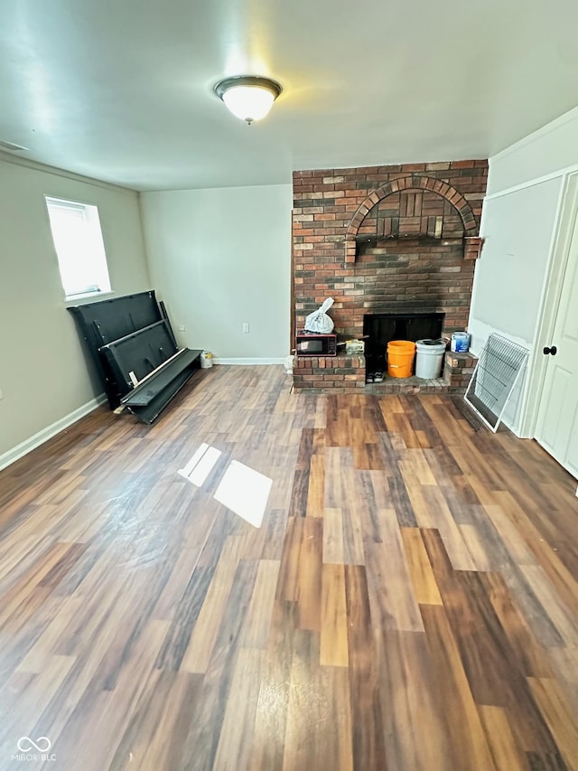 unfurnished living room with a brick fireplace, wood finished floors, and baseboards