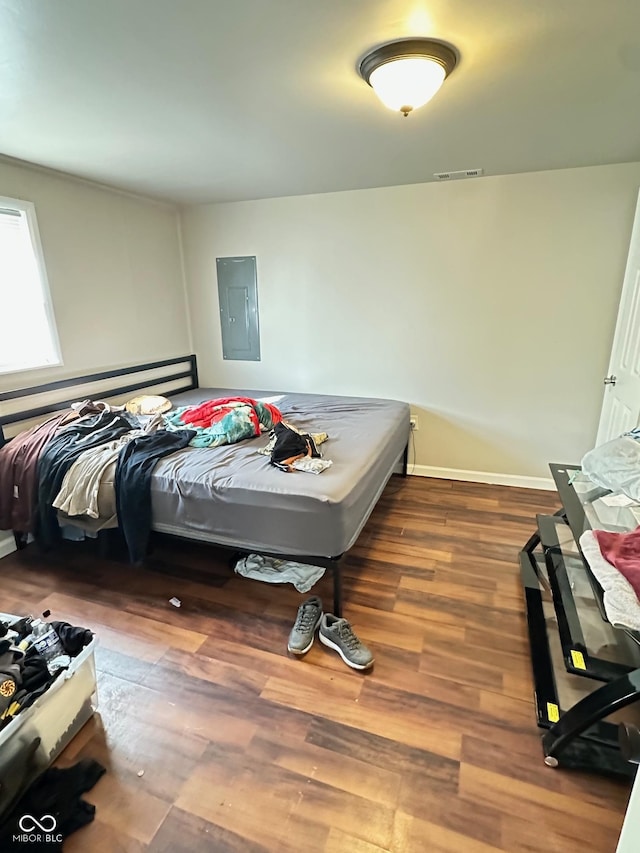 bedroom featuring electric panel, wood finished floors, visible vents, and baseboards