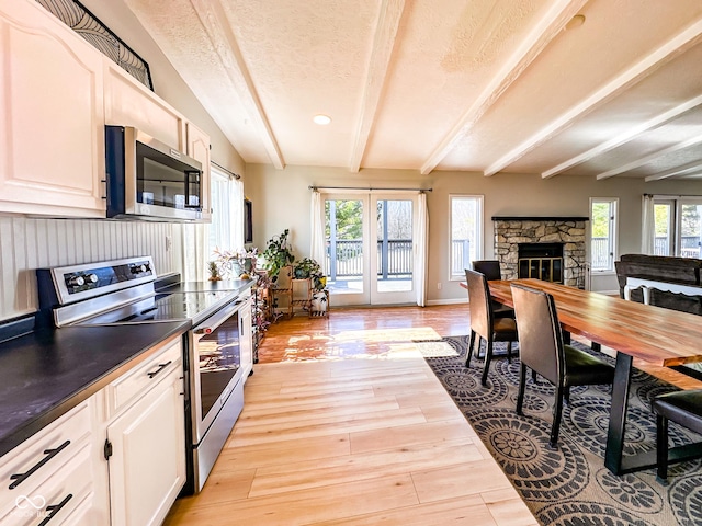 kitchen with dark countertops, light wood finished floors, beamed ceiling, a fireplace, and stainless steel appliances