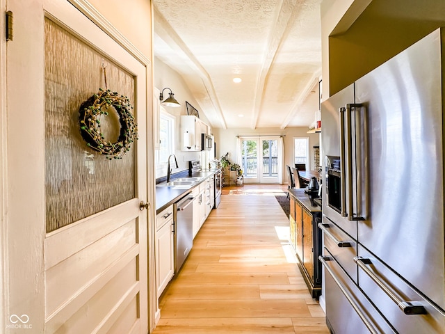 kitchen with light wood finished floors, beam ceiling, stainless steel appliances, a textured ceiling, and a sink